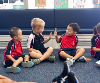 Two boys giving each other a high 5 while another boy looked on and a girl at the other side